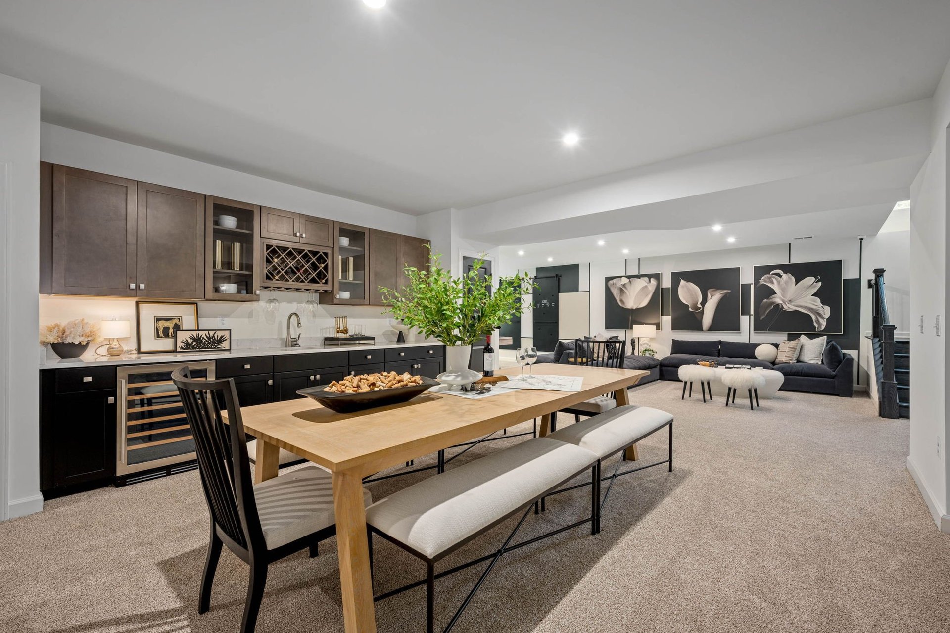 Modern open-concept basement with wood dining table, kitchen with dark cabinets, and lounge area with contemporary decor